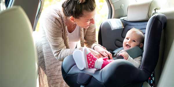 A mother setting her baby into a car seat in a car.